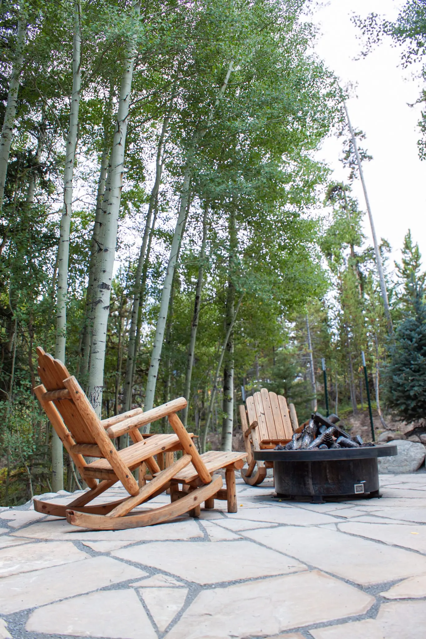 Fire pit and Adirondack seating area on a stone patio in an aspen grove