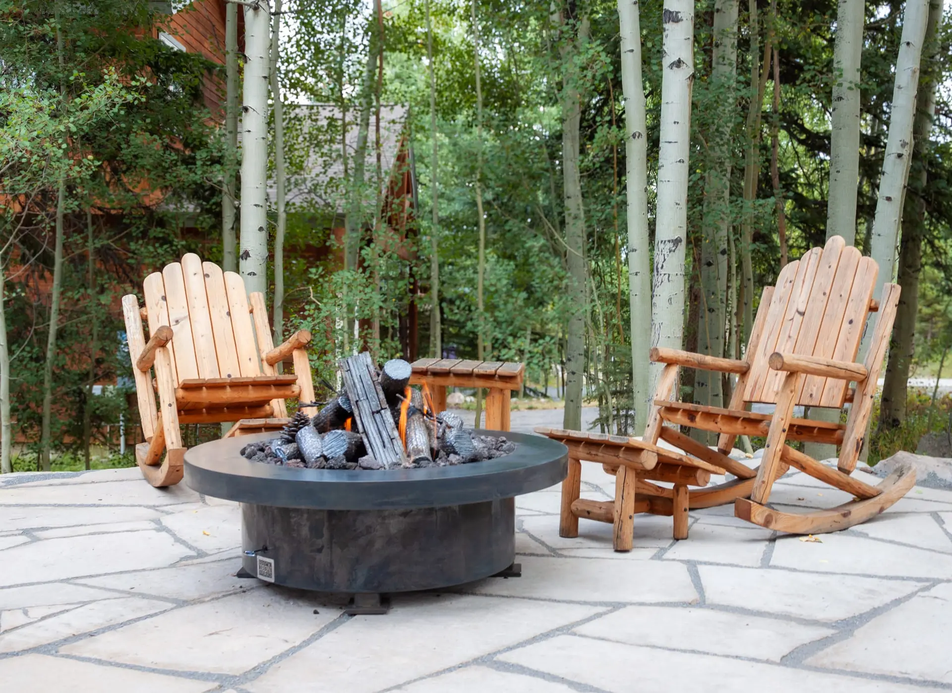Modern gas fire pit set into a paver patio surrounded by aspens